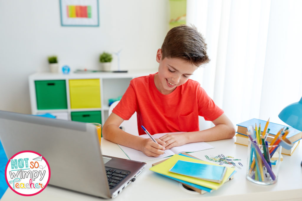 Boy in orange shirt with laptop, notebooks, pencils and books doing remote learning 
